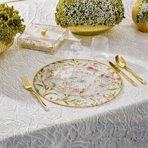 Decorative table setting with floral plate, gold cutlery, and small plants on a lace tablecloth.