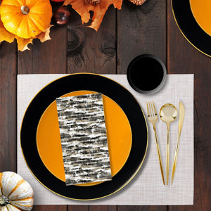 Table setting with black and orange plates, gold cutlery, and pumpkins on a wooden surface.