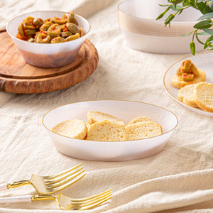 Table setting with a bowl of bread, a plate of olives, and gold forks on a beige tablecloth.