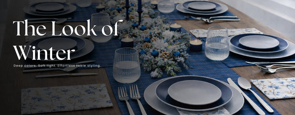 Winter-themed table setting with blue and gray plates, silverware, and decorative elements on a blue tablecloth.