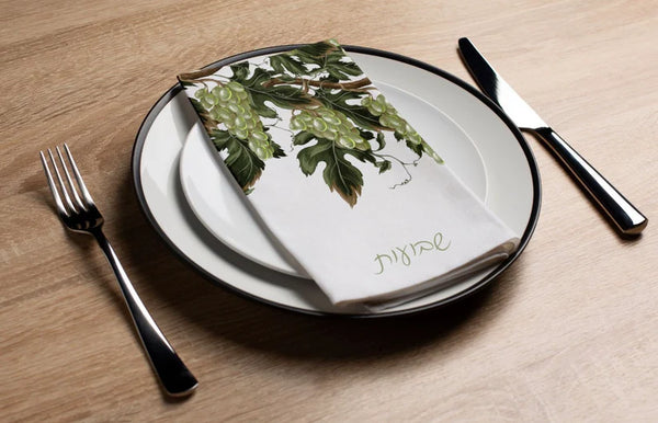 Table setting with a white plate, green leafy napkin, and silverware on a wooden surface.