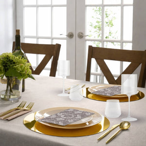 Dining table set with gold plates, silverware, and white napkins in a bright room.