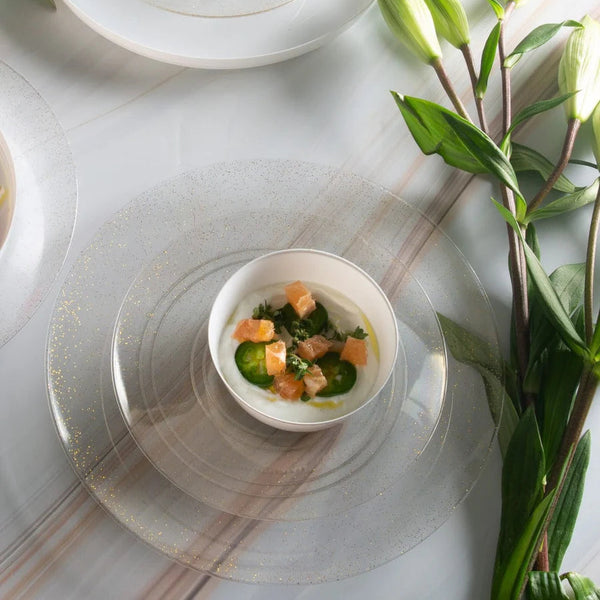 Dinner setting with white plates, gold cutlery, and greenery on a white tablecloth.