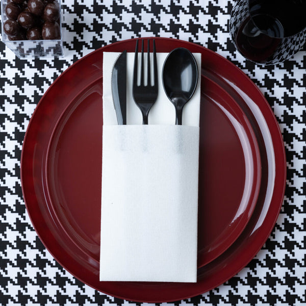 place setting of red plate with black and white tablecloth and flatware