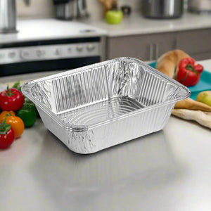 A shiny extra-deep 9x13 aluminum pan placed on a kitchen countertop, surrounded by fresh vegetables like tomatoes and bell peppers in a home kitchen setting.