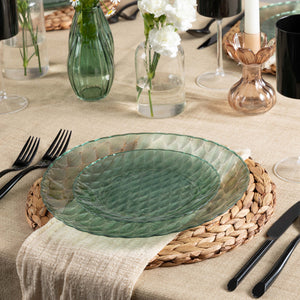 Green glass look plate on a woven placemat with cutlery and vases in the background
