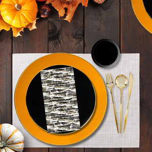 Thanksgiving table setting with orange plates, black bowls, gold cutlery, and pumpkins on a wooden table.