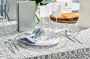 Passover seder table setting with patterned tablecloth, plates, disposable glasses, and cutlery.
