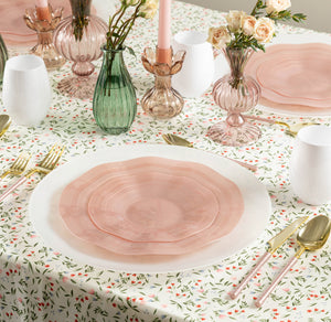 Dining table setting with pink plates, floral tablecloth, and decorative vases.