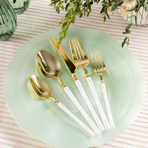 Gold cutlery set with pearl white handles on a green plate, placed on a textured surface with greenery.
