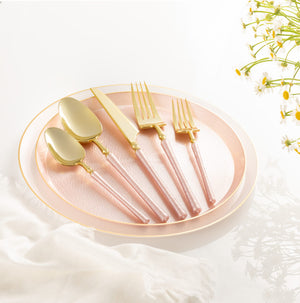 Set of pink plates with pink and gold cutlery on a white surface with flowers in the corner.