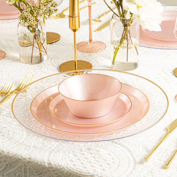 Table setting with pink plates, gold cutlery, and decorative elements on a white tablecloth.
