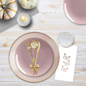 Dinner setting with pink plates, gold cutlery, and decorative elements on a wooden table.