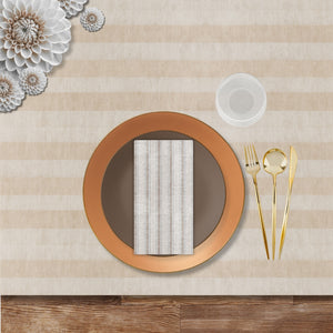 Fall-themed disposable dinnerware place setting with bronze charger, taupe plate, striped napkin, gold cutlery, and ribbed goblet on a neutral striped tablecloth.