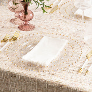 Elegant tablescape featuring a clear gold-beaded charger plate styled with gold flatware, textured linens, and soft pink glass decor.