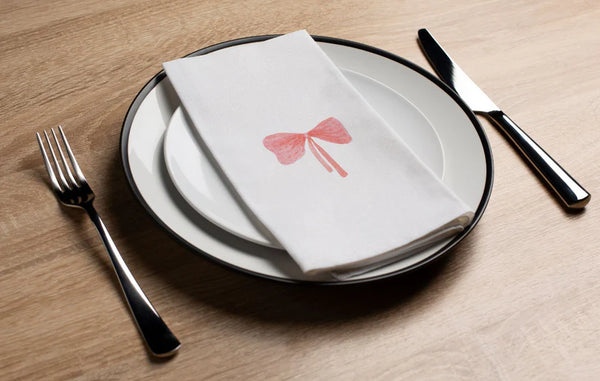 Dinner setting with a plate, folded napkin with a bow design, knife, and fork on a wooden table.