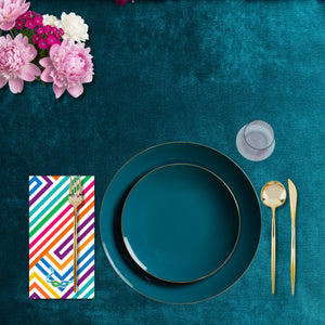 Teal plates with gold cutlery on a teal tablecloth, accompanied by pink flowers.