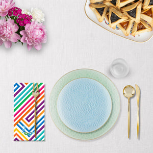 Dining purim table setting with a colorful striped napkin, light blue plate, and gold cutlery on a white surface.
