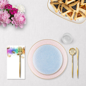 Dining table setting with a blue plate, pink rim, and gold cutlery on a white tablecloth.