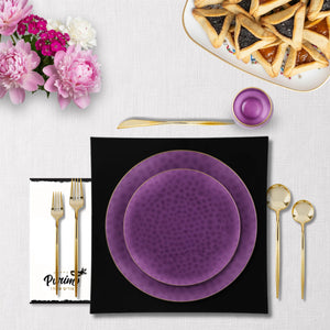 Purple plates with gold cutlery on a white tablecloth with flowers and pastries.