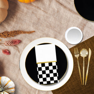 Table setting with a black plate, checkered napkin, and gold cutlery on a textured surface.