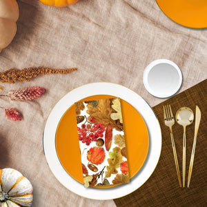 Table setting with a decorative napkin featuring autumn leaves on a white plate, surrounded by pumpkins and fall-themed decor.