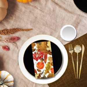 Table setting with a floral napkin on a white plate, surrounded by autumn-themed decor.